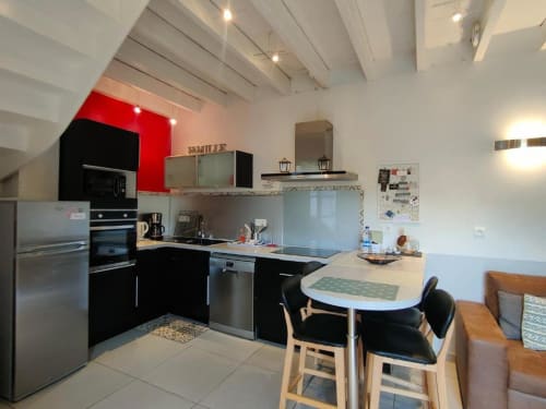 Cuisine contemporaine avec armoires noires, mur d'accent rouge, appareils inox et table à manger au Gîte de la Tannerie, Dinan