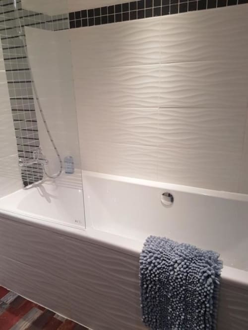 Salle de bains moderne avec baignoire blanche, douche vitrée et carrelage texturé à La Conciergerie de Nathalie, Dinan