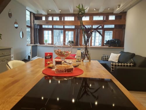 Salle à manger de l'appartement Ty Clement à Dinan avec table en bois, vue sur la ville par grandes fenêtres et mobilier moderne