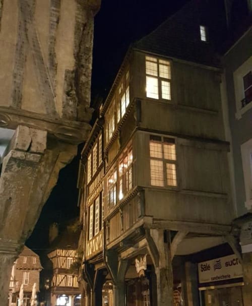 Bâtiments historiques à colombages illuminés la nuit à Dinan, France, avec fenêtres éclairées et architecture traditionnelle