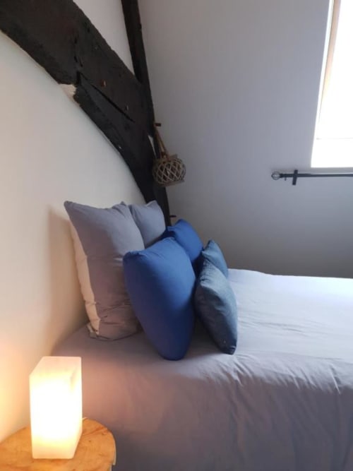 Chambre moderne à La Conciergerie de Nathalie à Dinan avec oreillers bleus sur literie blanche et éclairage ambiant
