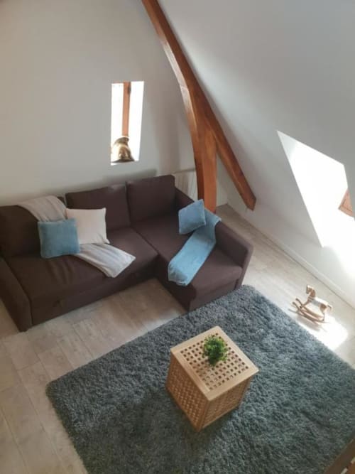 Salon douillet d'appartement mansardé à Dinan avec canapé sombre, accents bleus, poutres en bois et lumière naturelle