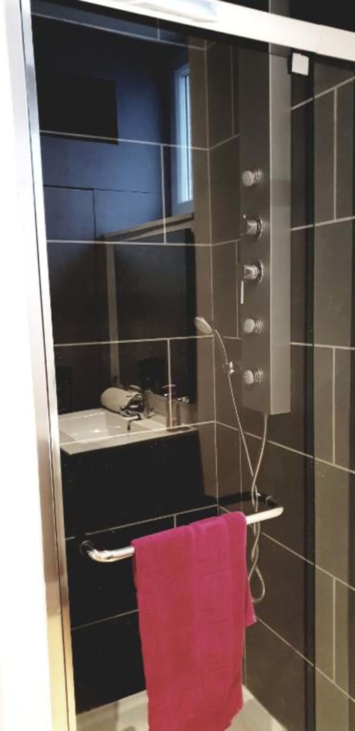 Élégante douche à carrelage noir avec pluie de tête et jets corporels multiples à La Conciergerie de Nathalie