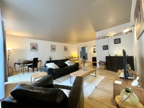 Spacieux séjour de duplex à Dinan avec canapés en cuir noir, parquet, table à manger et coin TV