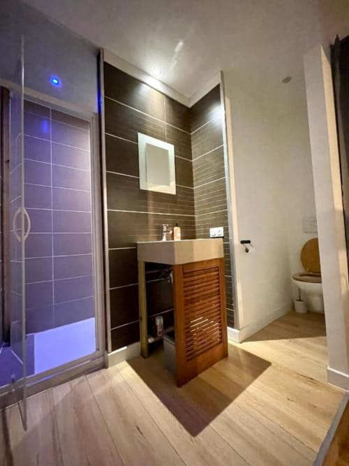 Salle de bain moderne du duplex La Conciergerie de Nathalie à Dinan avec carrelage noir, meuble vasque en bois et douche