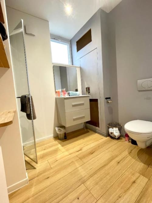 Salle de bains moderne de l'appartement duplex La Conciergerie de Nathalie à Dinan, avec vasque blanche, toilettes, douche et parquet.
