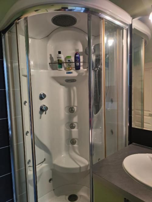 Cabine de douche moderne avec paroi vitrée, pommeau de douche pluie et jets corporels à La Conciergerie de