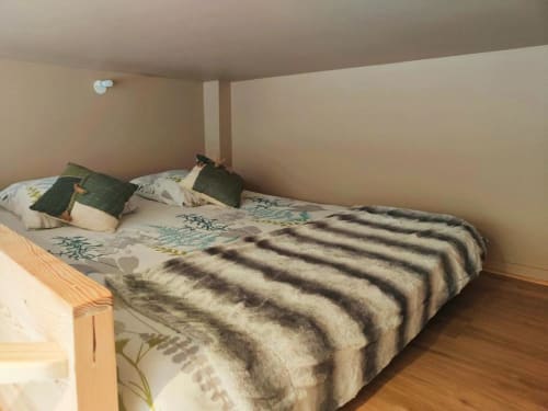 Chambre cosy à Dinan avec couverture rayée, coussins verts, parquet et plafond mansardé