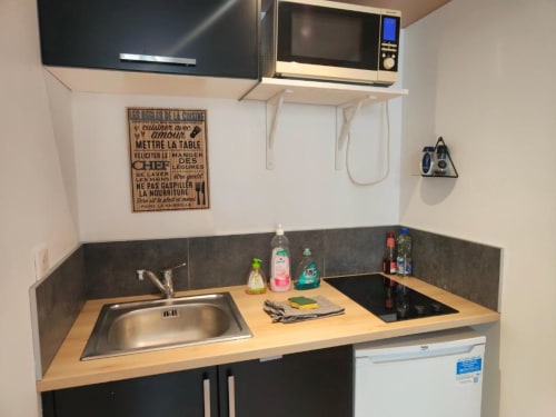 Petite kitchenette du Studio Hikoki à La Conciergerie de Nathalie, Dinan, équipée d'un évier, cuisinière, micro-ondes et rangements.