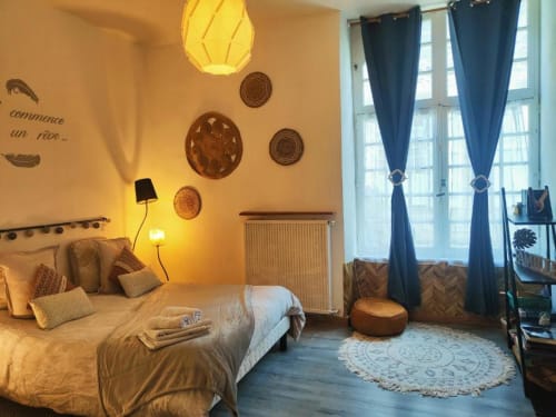 Chambre douillette à La Conciergerie de Nathalie, Dinan. Lumière chaleureuse, assiettes décoratives, lit avec oreillers et coin salon