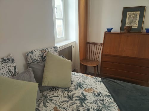 Chambre douillette à La Conciergerie de Nathalie, Dinan avec lit, commode en bois, fauteuil et vue sur la ville