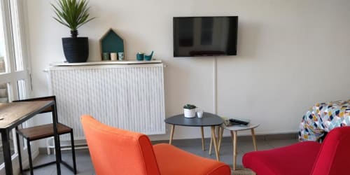 Studio de jardin moderne à La Conciergerie de Nathalie à Dinan avec fauteuil orange, canapé rouge, TV murale et design minimaliste