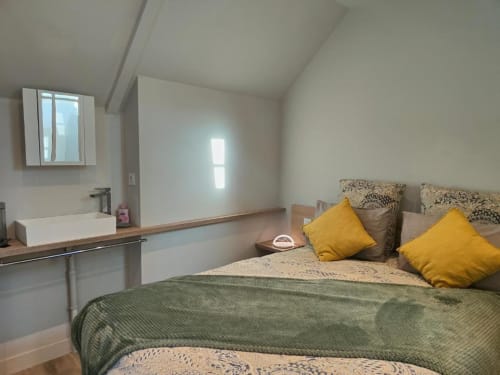 Chambre moderne de la Villa Hortense à Dinan avec literie verte, oreillers jaunes et salle de bain attenante avec vue sur la ville
