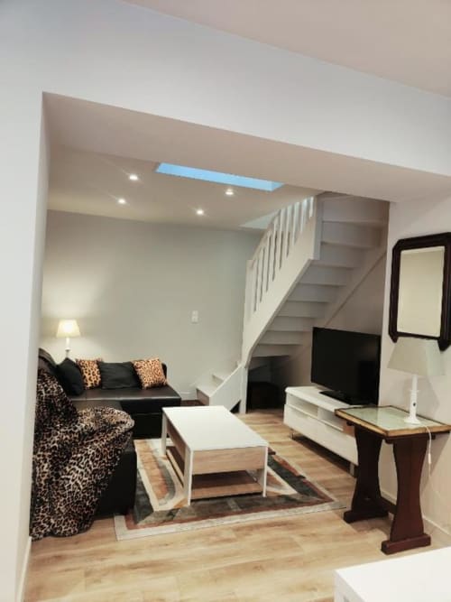 Studio moderne avec canapé noir, fauteuil léopard, parquet, lucarne et escalier à La Conciergerie de