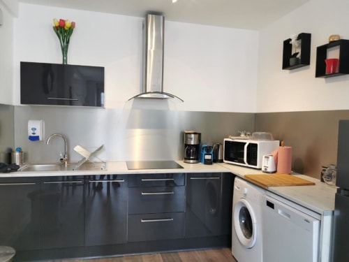 Cuisine moderne dans un appartement de Dinan avec électroménager inoxydable, armoires sombres et buanderie compacte