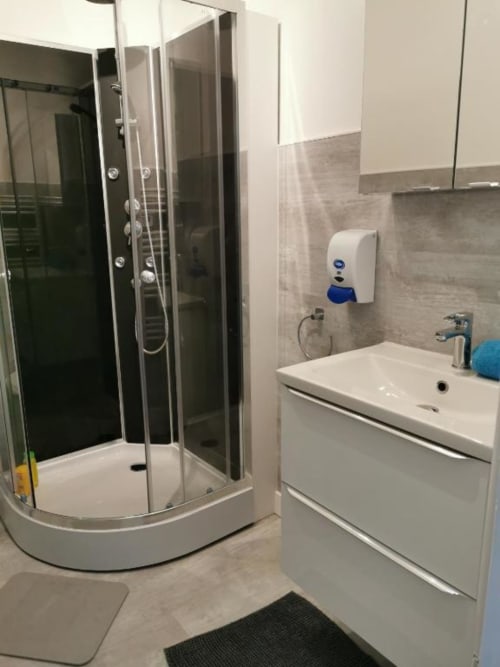 Salle de bain moderne dans un appartement à Dinan avec douche en verre incurvé, vasque blanche et distributeur de savon mural