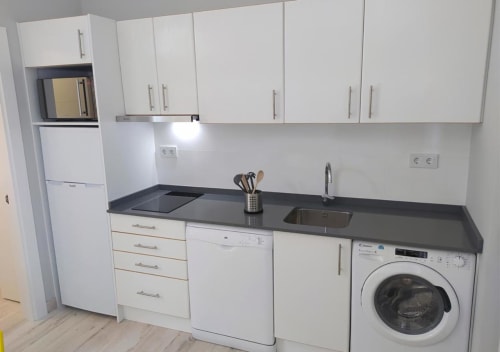 Modern kitchenette at Hotel Santorini Belgrade with white cabinets, black countertop, sink, washing machine, and appliances