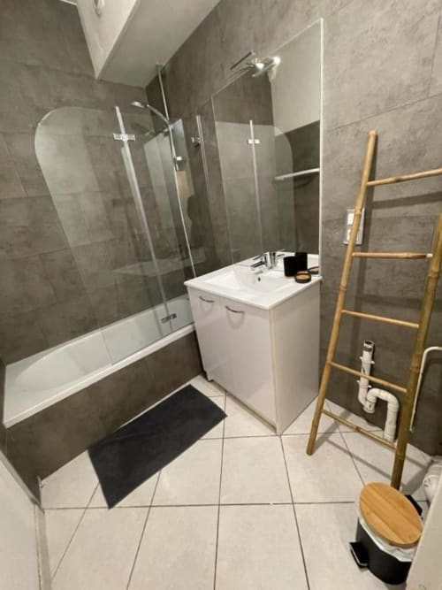 Salle de bain moderne à La Conciergerie de Nathalie à Dinan avec vasque blanche, carrelage gris, baignoire, douche vitrée et