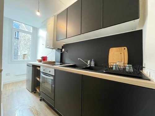 Cuisine moderne noire avec plan de travail en bois, évier, four et fenêtre dans l'appartement de Dinan à La Conciergerie de Nathalie