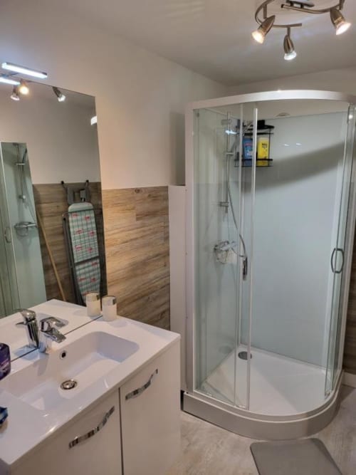 Salle de bain moderne à La Conciergerie de Nathalie à Dinan avec lavabo blanc, douche vitrée et accent bois
