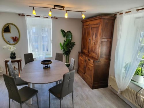 Élégante salle à manger à La Conciergerie de Nathalie à Dinan avec table ronde, armoire en bois et éclairage moderne.