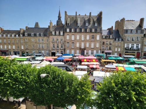 Place de marché colorée à Dinan avec architecture en pierre et étals de vendeurs