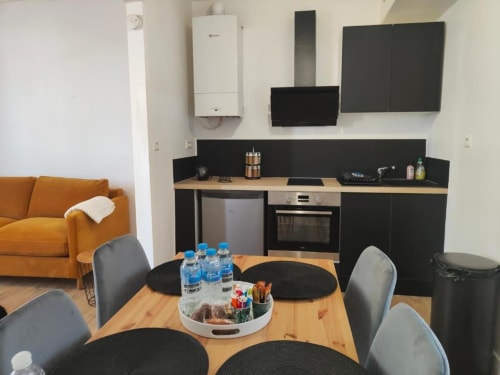 Cuisine et salle à manger modernes avec canapé orange, meubles noirs et table en bois à Dinan
