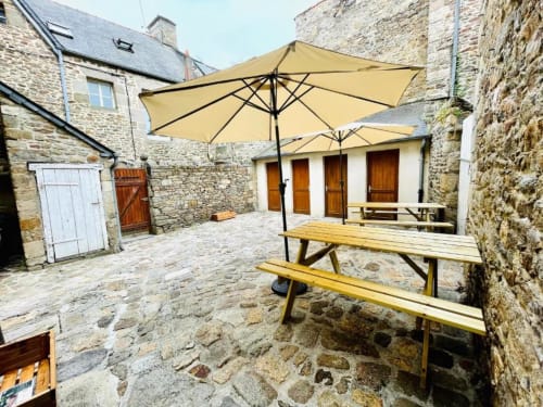 Cour avec parasols jaunes et tables de pique-nique en bois à La Conciergerie de Nathalie à Dinan, France
