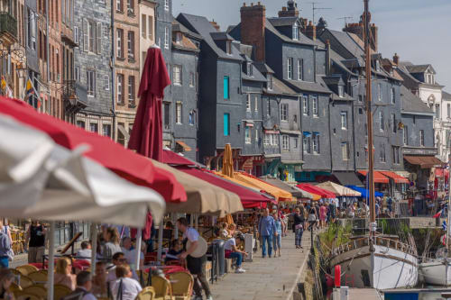 Marché animé du port de Honfleur avec ses tentes rayées rouges, bâtiments historiques et bateaux amarrés le long du bassin
