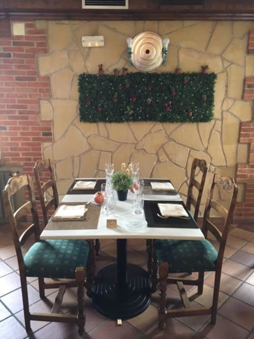 Elegant dining room at Hotel Santorini Belgrade with stone fireplace, set table for two, and decorative hedging
