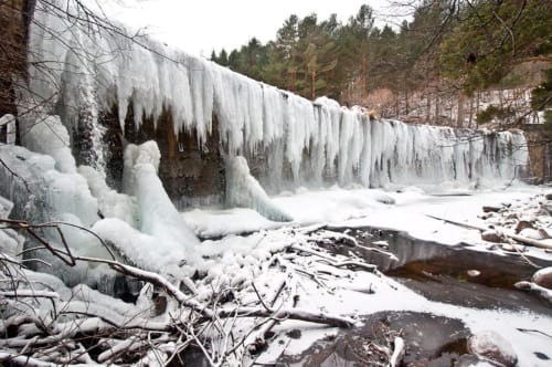 Frozen waterfall with icy formations and snow-covered landscape in winter forest setting