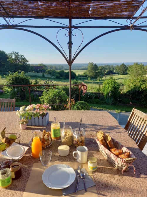 Table de petit-déjeuner avec vue sur la campagne française à La Maison De Fleurat, Domeyrot, avec viennoiseries, jus et fleurs