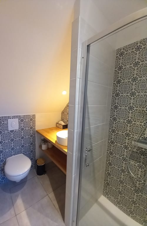 Salle de bain moderne de la villa La Maison De Fleurat avec carrelage à motifs, toilettes, meuble vasque en bois et douche vitrée