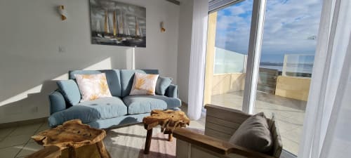 Salon moderne au Relais des Îles avec vue mer, canapé bleu, tables en bois et portes-fenêtres donnant sur la terrasse