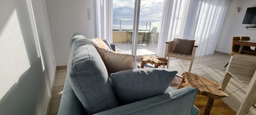 Lumineux salon côtier avec vue sur mer aux Relais des Îles, Saint-Marcouf. Canapé gris, mobilier en bois, portes vitrées