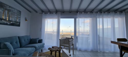 Salon moderne du gîte avec canapé bleu, terrasse vue mer et baies vitrées à Relais des Îles, Saint-Marcouf