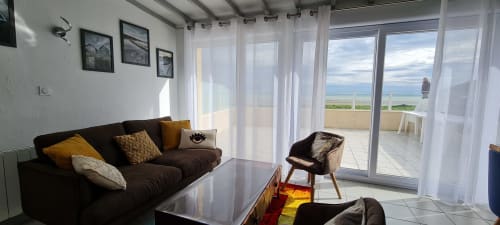 Modern cottage living room with sea view terrace at Relais des Iles, Saint-Marcouf. Brown sofa, coastal décor, large windows