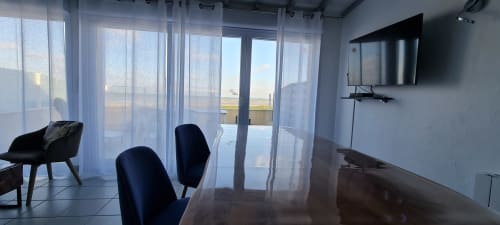 Spacious cottage living room with sea view, dining table, black chairs, TV, and glass doors opening to terrace at Relais des