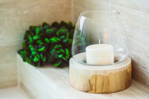 Elegante candelabro in legno con candela pillar bianca e paralume in vetro accanto a una succulenta verde su mensola in marmo