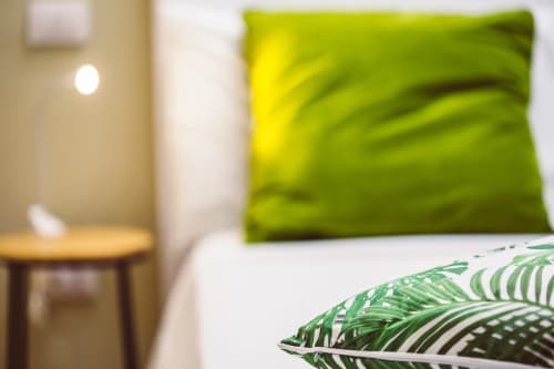 Stylish double bed with lime green pillow and tropical leaf patterns at Bluemoon Sardinia, Cagliari