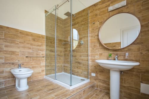 Modern bathroom in Bluemoon Sardinia's Double King Room in Cagliari with wood-tile walls, rainfall shower, pedestal sink, and
