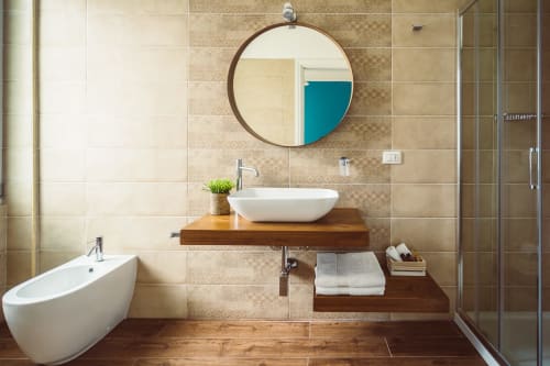 Modern bathroom at Bluemoon Sardinia Cagliari with vessel sink, round mirror, wooden vanity, and walk-in shower