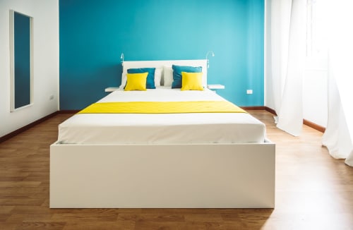 Modern double bedroom at Bluemoon Sardinia with turquoise accent wall, yellow bedding, white bed frame, and wooden floors in