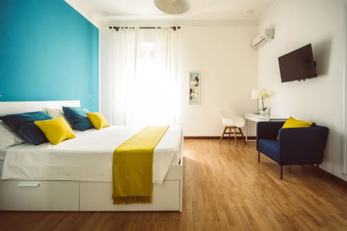 Modern double room at Bluemoon Sardinia with turquoise accent wall, white bed, yellow accents, desk, armchair, and