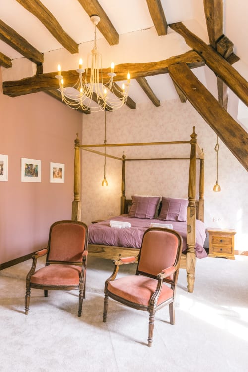 Elegant bedroom at Le Prieuré Du Preux with exposed beams, canopy bed, chandelier, and garden view