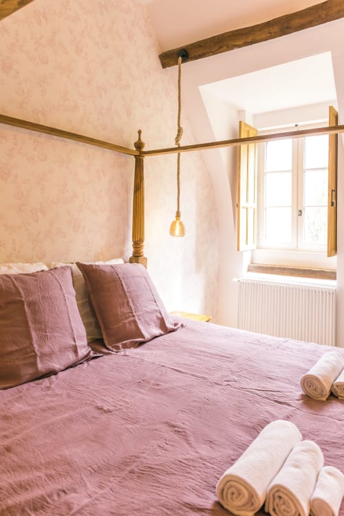 Lit à baldaquin élégant avec lin rose dans la chambre Les Clos au Le Prieuré Du Preux, gîte français avec vue sur jardin