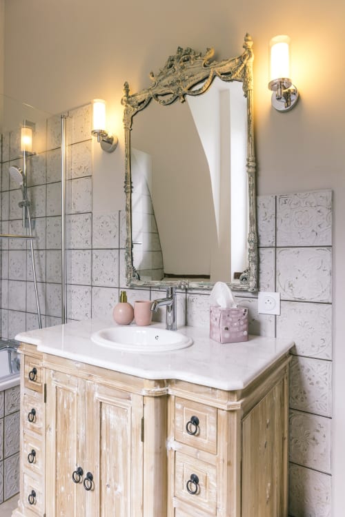 Élégante salle de bains du Prieuré Du Preux avec miroir orné, lavabo en marbre, meuble vasque en bois et carrelage décoratif