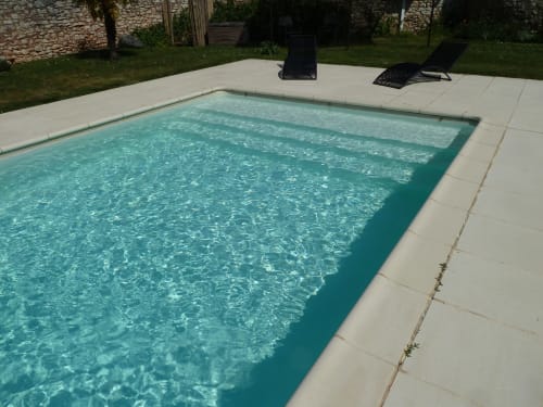 Piscina rectangular de aguas cristalinas en Château De Clusors con tumbonas y muros de piedra en Saint-Menoux, Francia