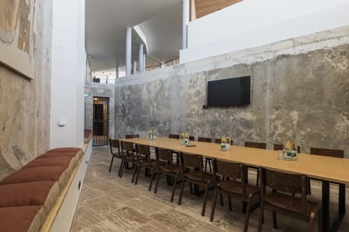 Salle de réunion moderne à l'Hôtel La Prison à Béziers avec table en bois massif, chaises noires et murs en béton brut