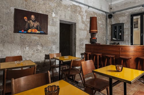 Comedor del Hotel La Prison en Béziers con mesas amarillas, sillas de madera, decoración vintage y paredes de piedra vista